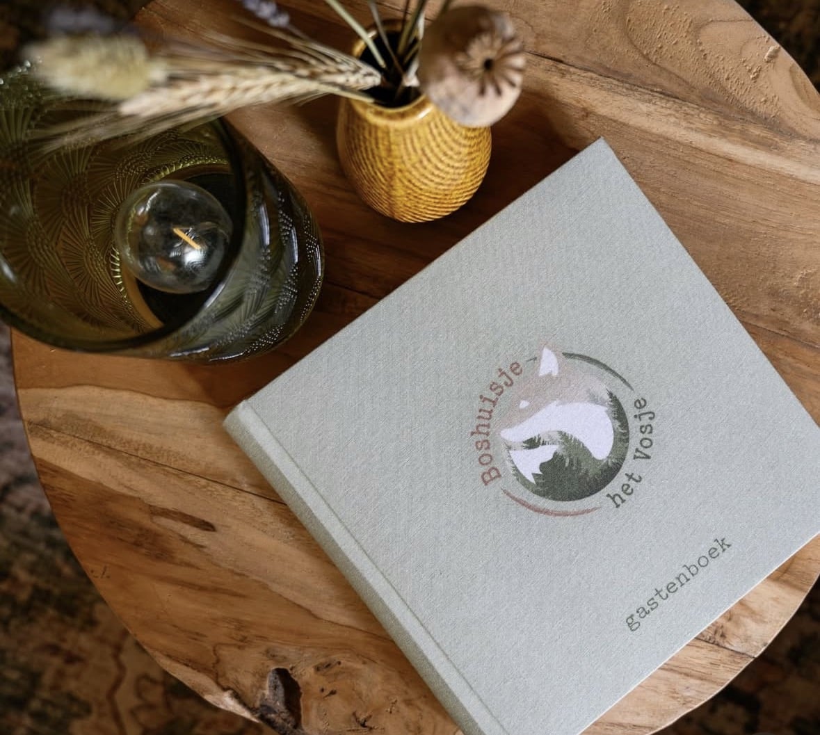 Gepersonaliseerd linnen gastenboek voor vakantiehuis of B&B, met naam op de kaft, liggend op een houten tafel in interieursetting